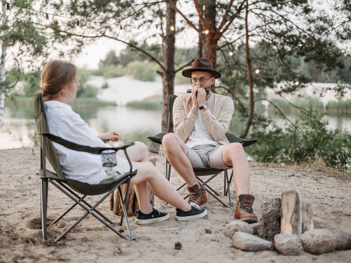Two people sitting in camp chairs beside a lakeside fire ring — Seat & Stake, camping chairs, cots & camp furniture