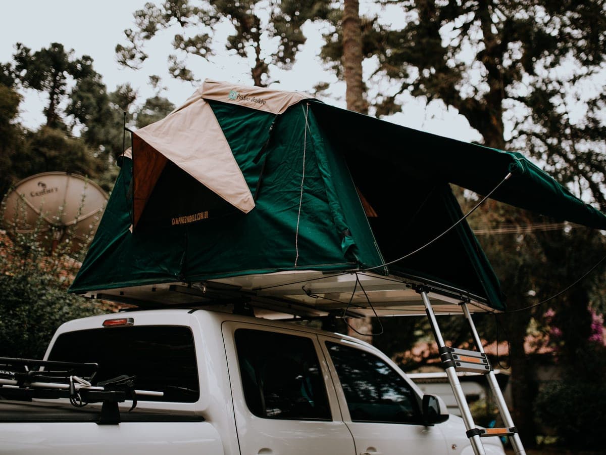 A rooftop tent set up on a pickup truck parked under trees